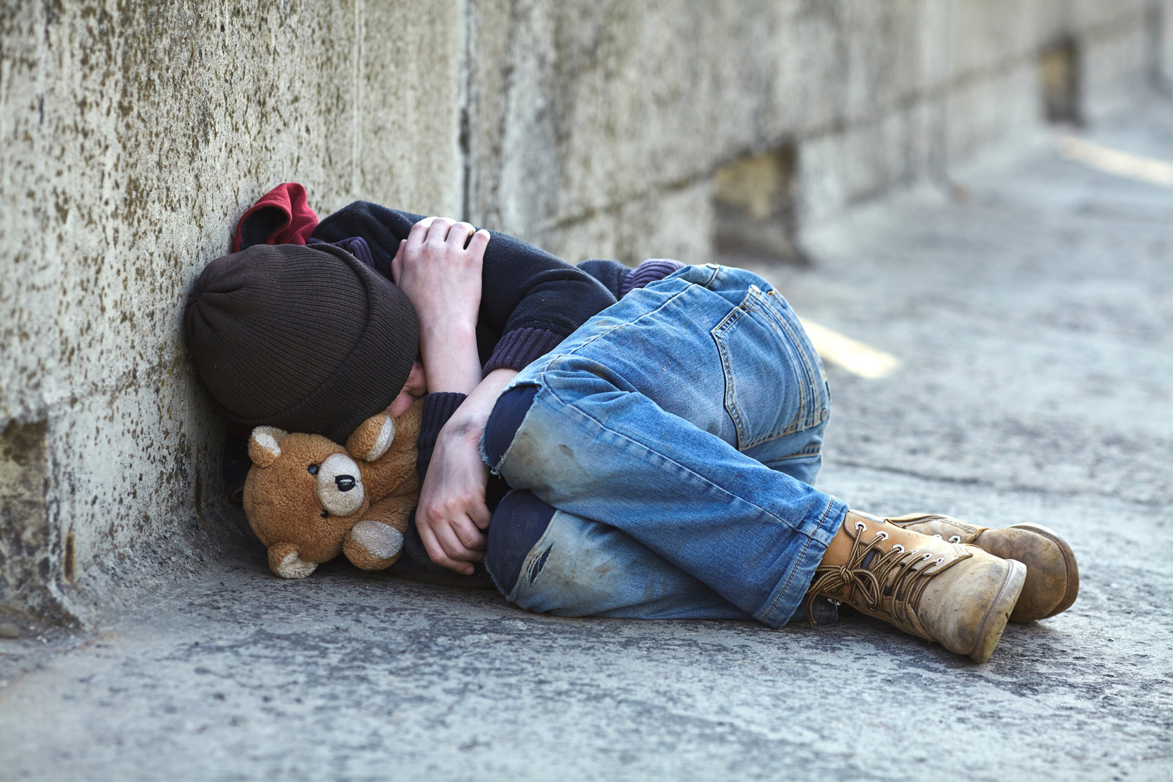 Child laying on ground with teddy bear in his arms